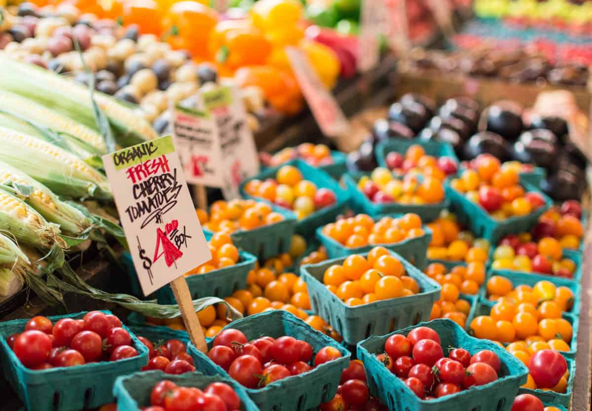Photo of a produce stall selling corn, and red and orange tomatoes.