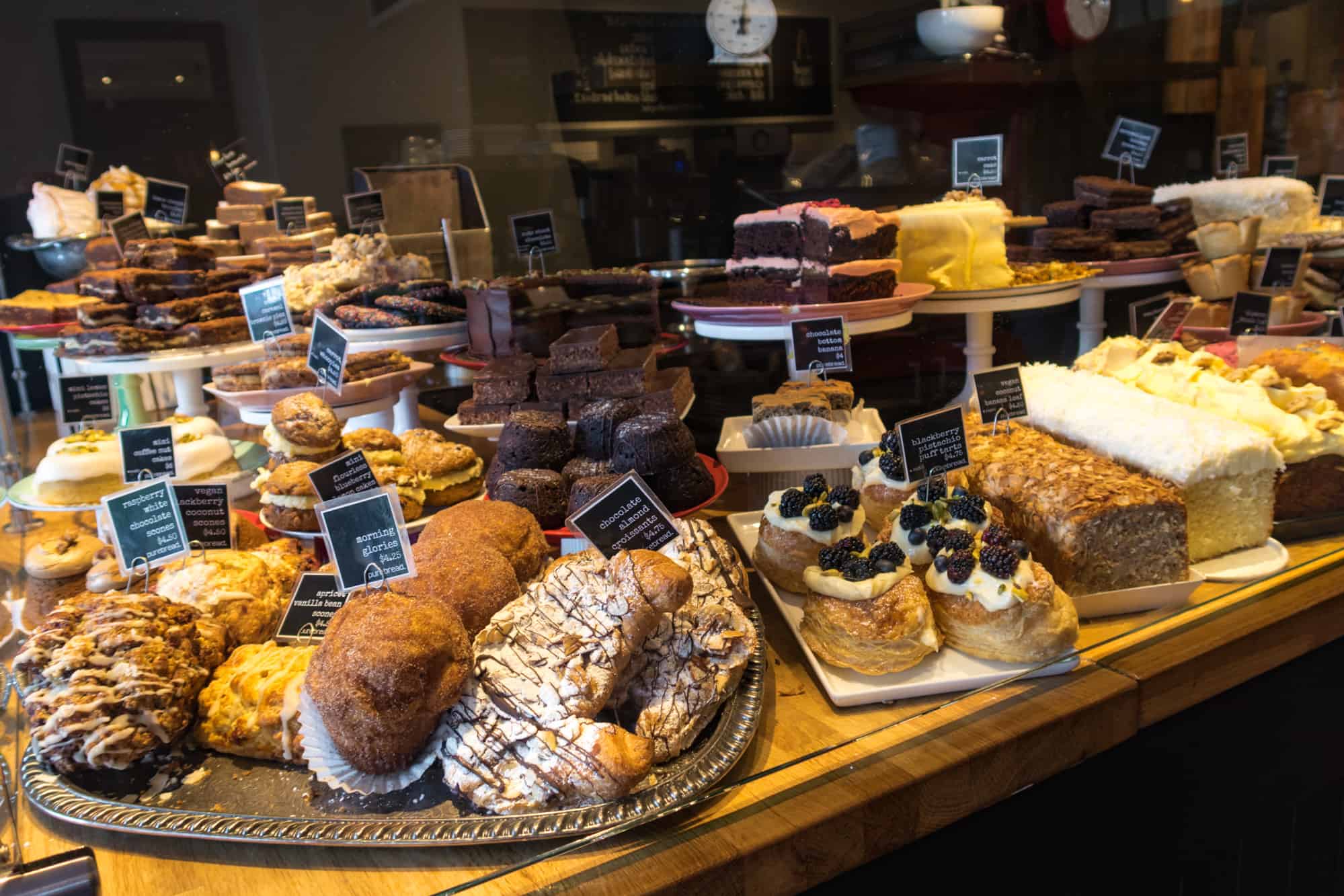 Photo of a counter filled with cakes and pastries such as scones, bars, loafs and croissants.
