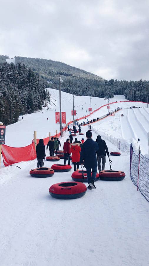 Photo of a group of people lining up with red inflatable tubes. The Tube Park in Whistler is a great family friendly activity. 