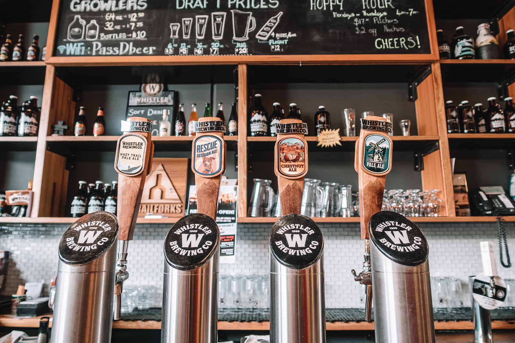Photo of four beer taps with a bar in the background lined with beer glasses and growlers.