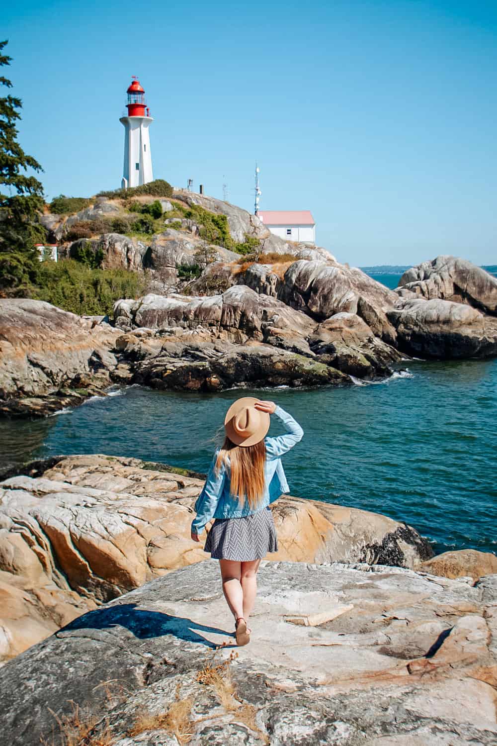 Rachael standing on a rocky outcrop and walking towards a lighthouse in the distance at Lighthouse Park, West Vancouver.