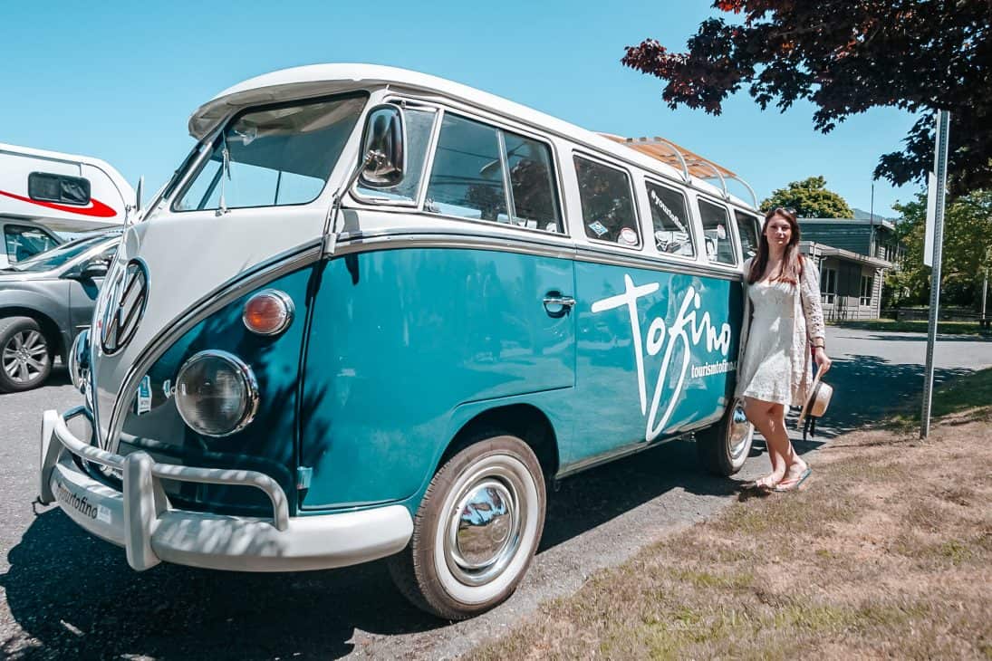 The Tofino VW - a volkswagen camper van with the Tofino logo on the front and a brown-haired girl standing in front of it