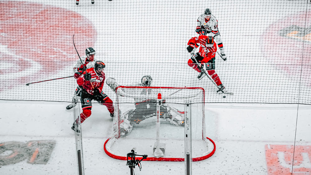 Photo of an ice rink with four hockey players, two wearing a red jersey and two wearing a white jersey, holding hockey sticks with a goalie standing in the goal.

A hockey game is one of the best Vancouver rainy day activities.