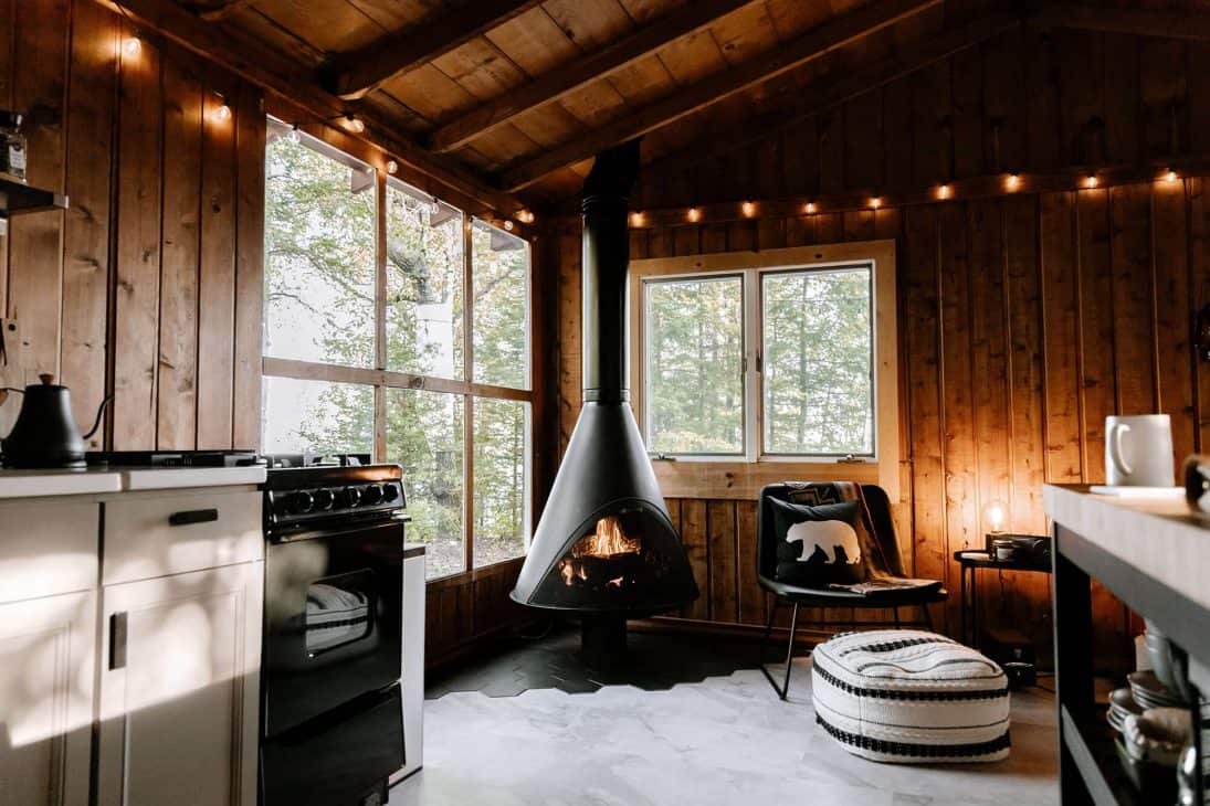 Photo of a cabin with a wood burning stove, fairy lights and cushions. 