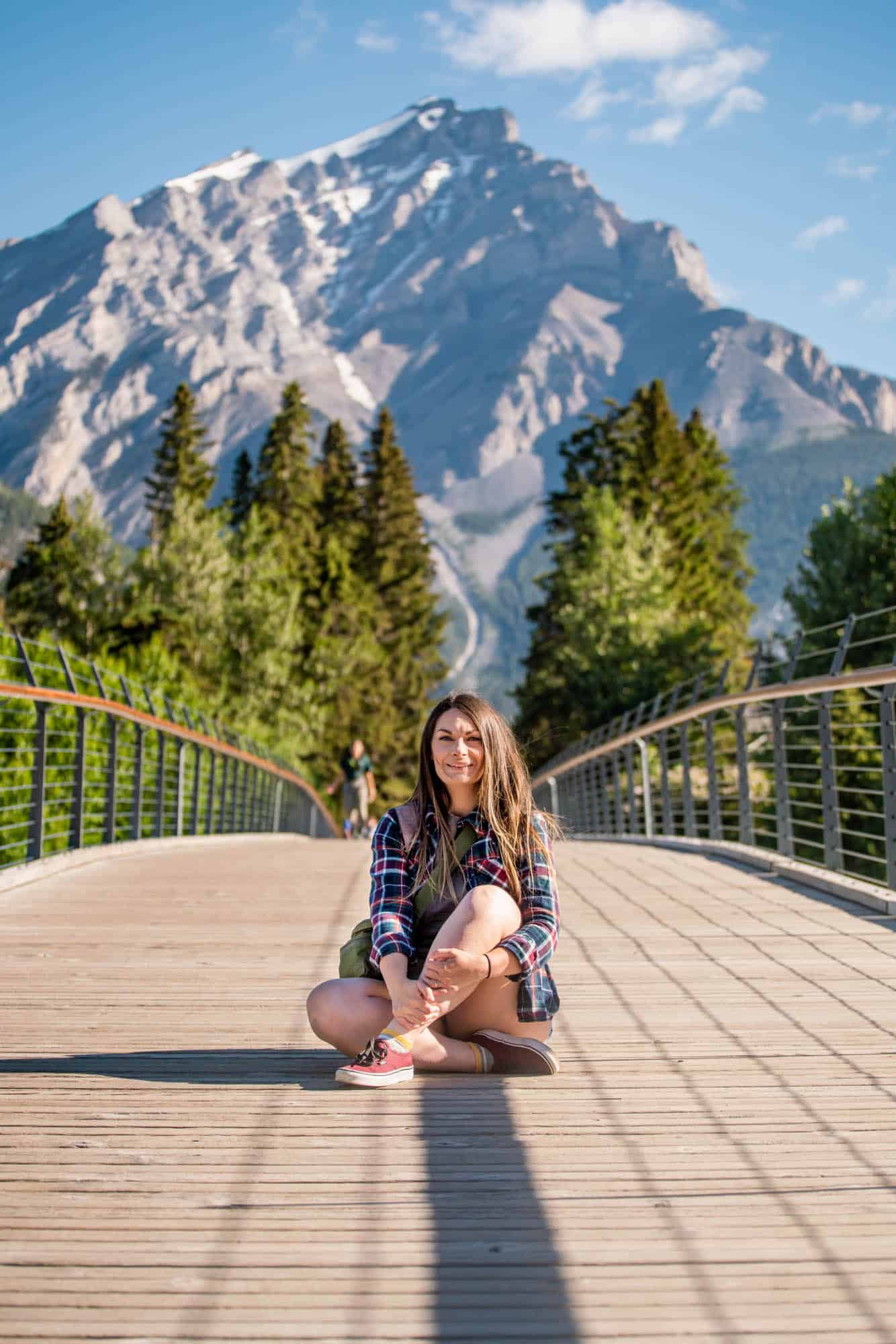 Rachael sitting on the Banff pedestrian Bridge with Cascade Mountain in the background.