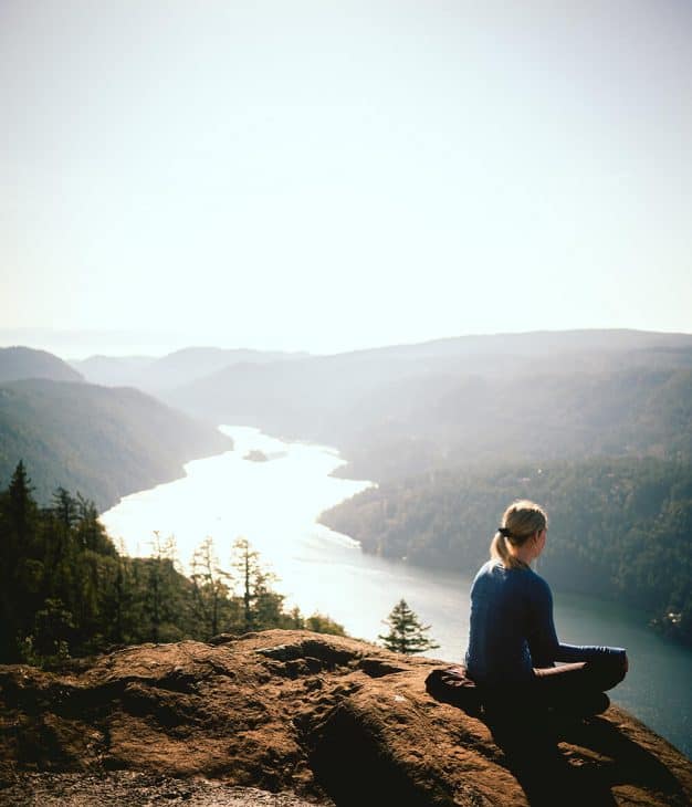 Jocelyn Hill hike in Victoria, BC. A woman sits on a rocky area with mountains in the background and a fjord. 