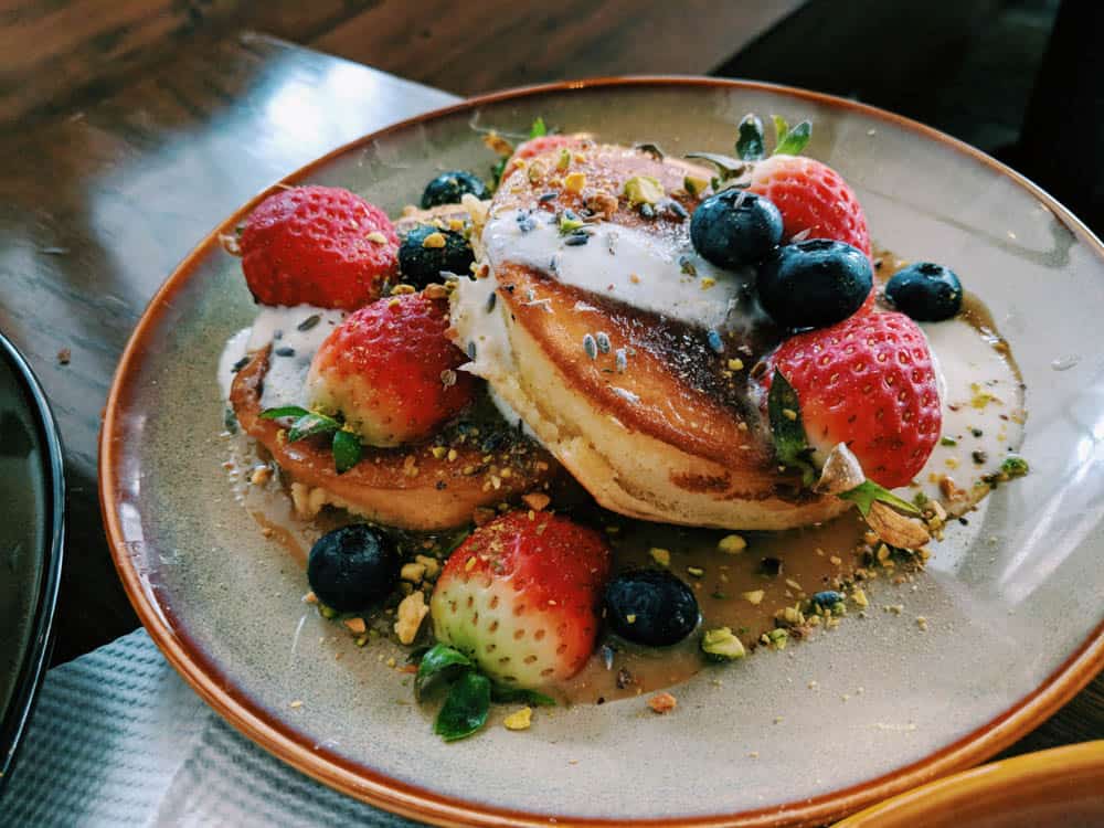 Close up photo of pancakes covered in nuts, strawberries, blueberries and cream.