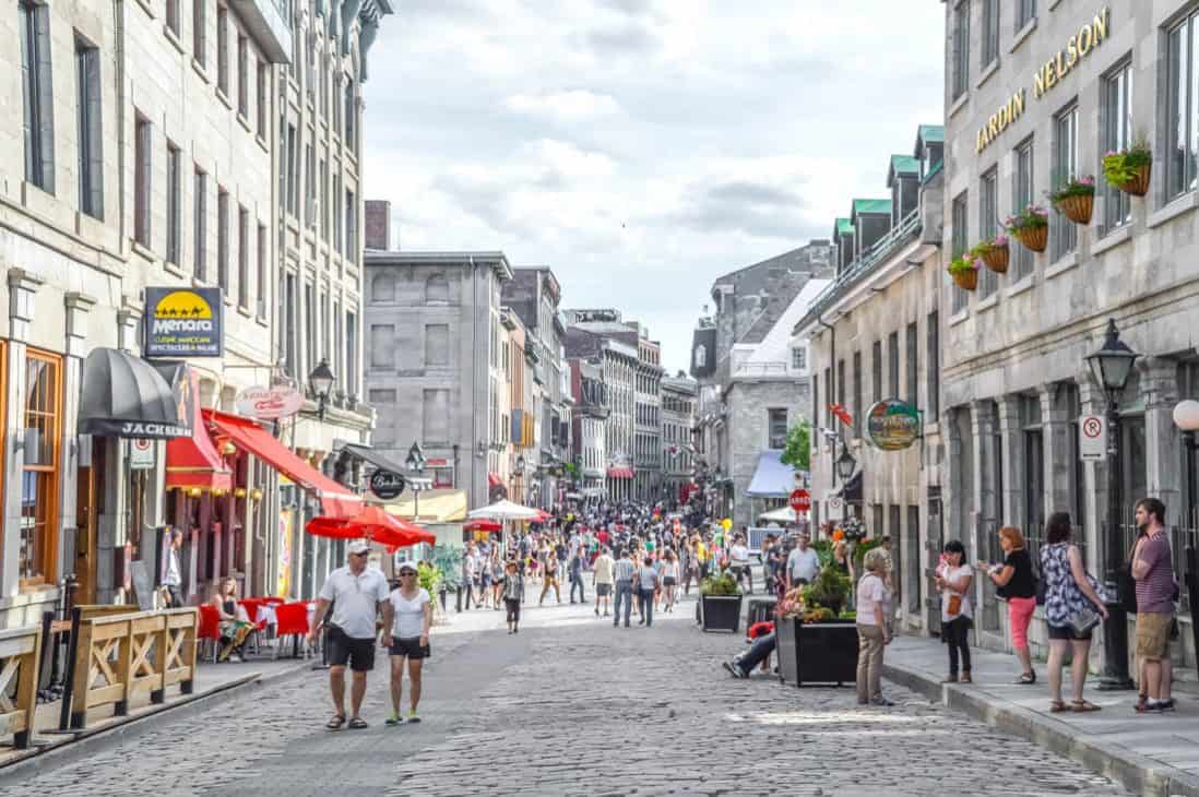 A cobbled stoned street filled with old style buildings on either side with people walking up and down the street. 
