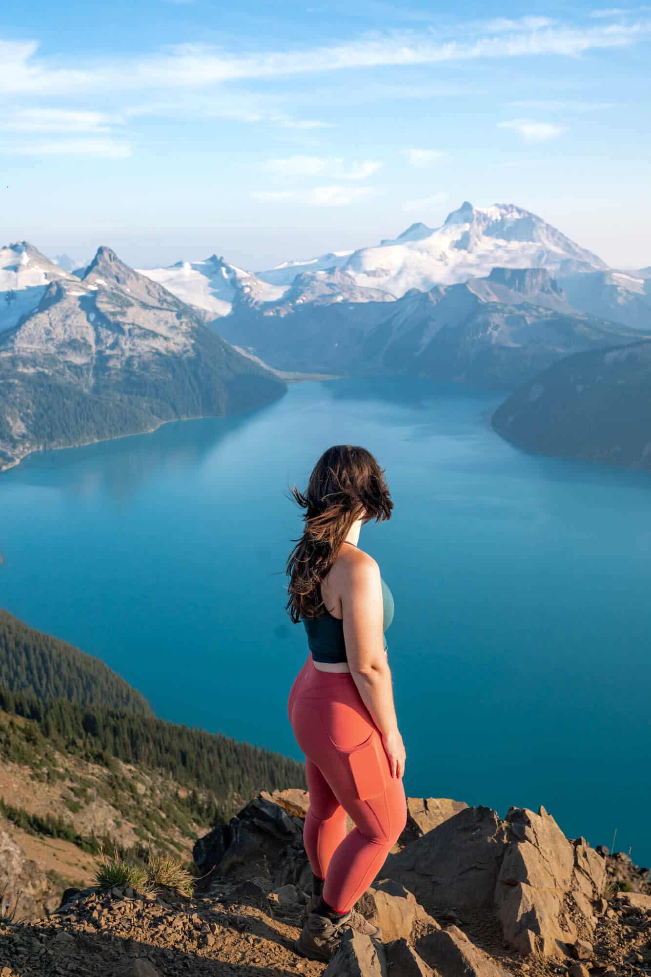 Photo of a woman looking out towards snow-capped mountains and a bright blue lake below. The Panorama Ridge hike is one of the best things to do in Whistler in winter.