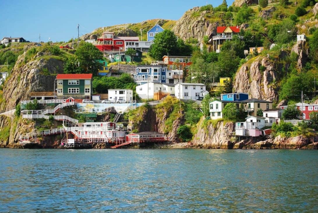 Photo of a rocky cliffside with colourful houses scattered throughout and the ocean in the foreground.