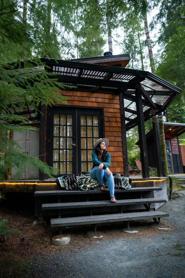 Woman sitting on the stairs of a rustic cabin in the forest.