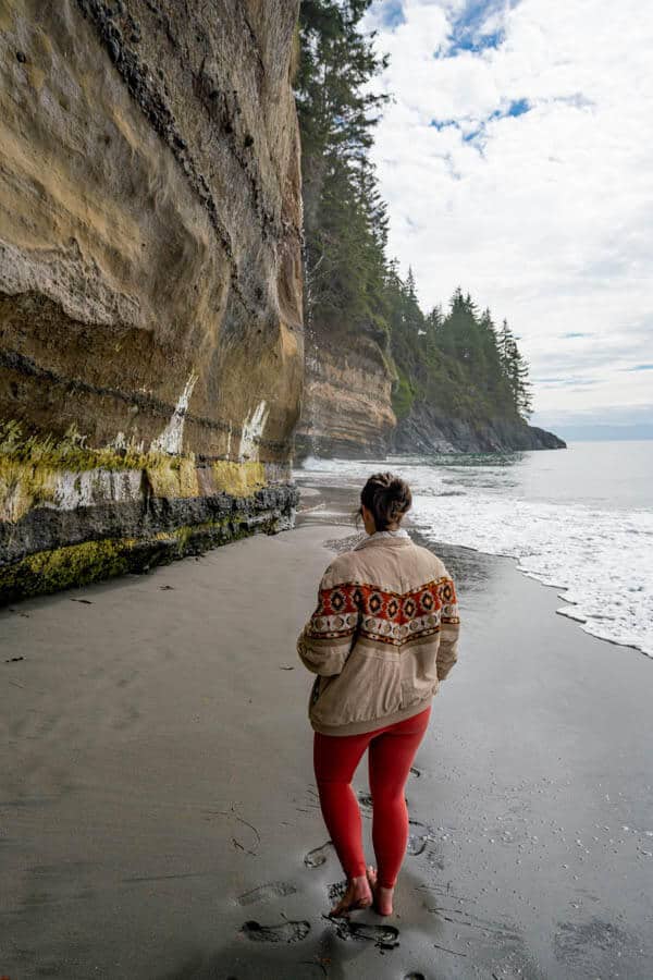 Photo of a woman standing on a beach with a cliffside on her left and ocean on the right. 