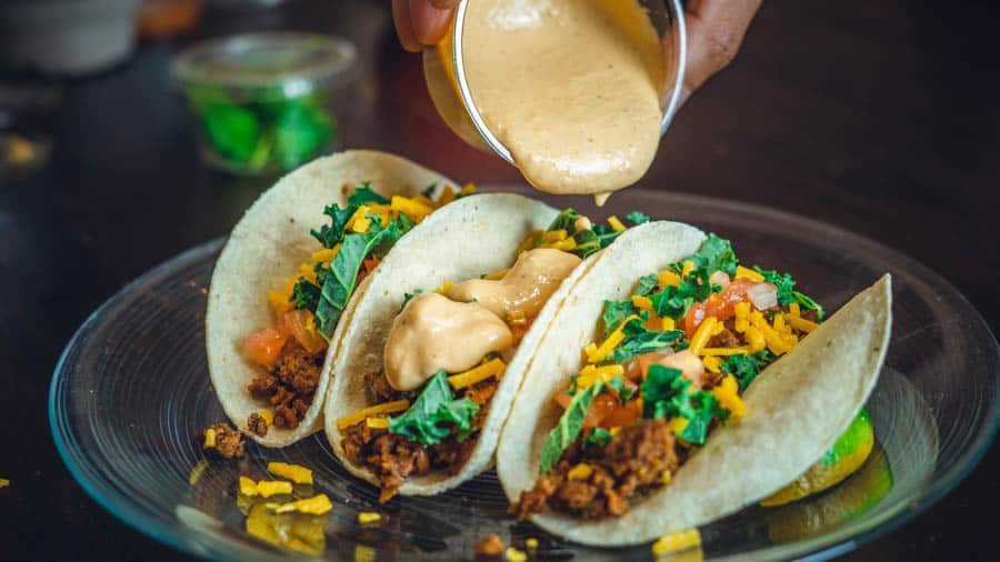 Photo of 3 corn tortilla tacos with ground beef cheese, onion, tomato and shredded lettuce. La Cantina has a taco Tuesday deal which makes it one of the top budget friendly eateries in Whistler.