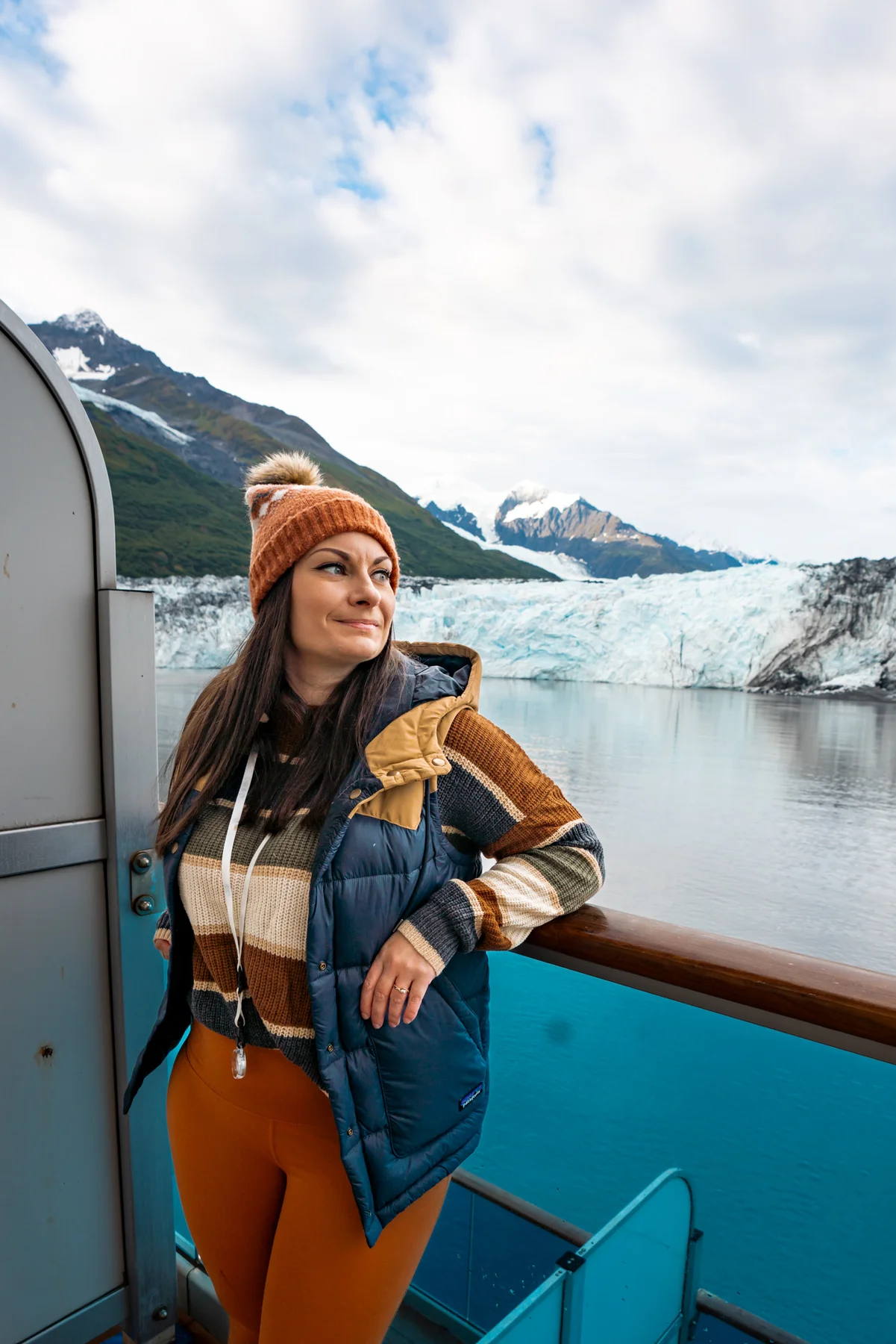 Rachael standing on a cruise ship balcony with a glacier behind. Booking a balcony is one of the best Alaska cruise tips.